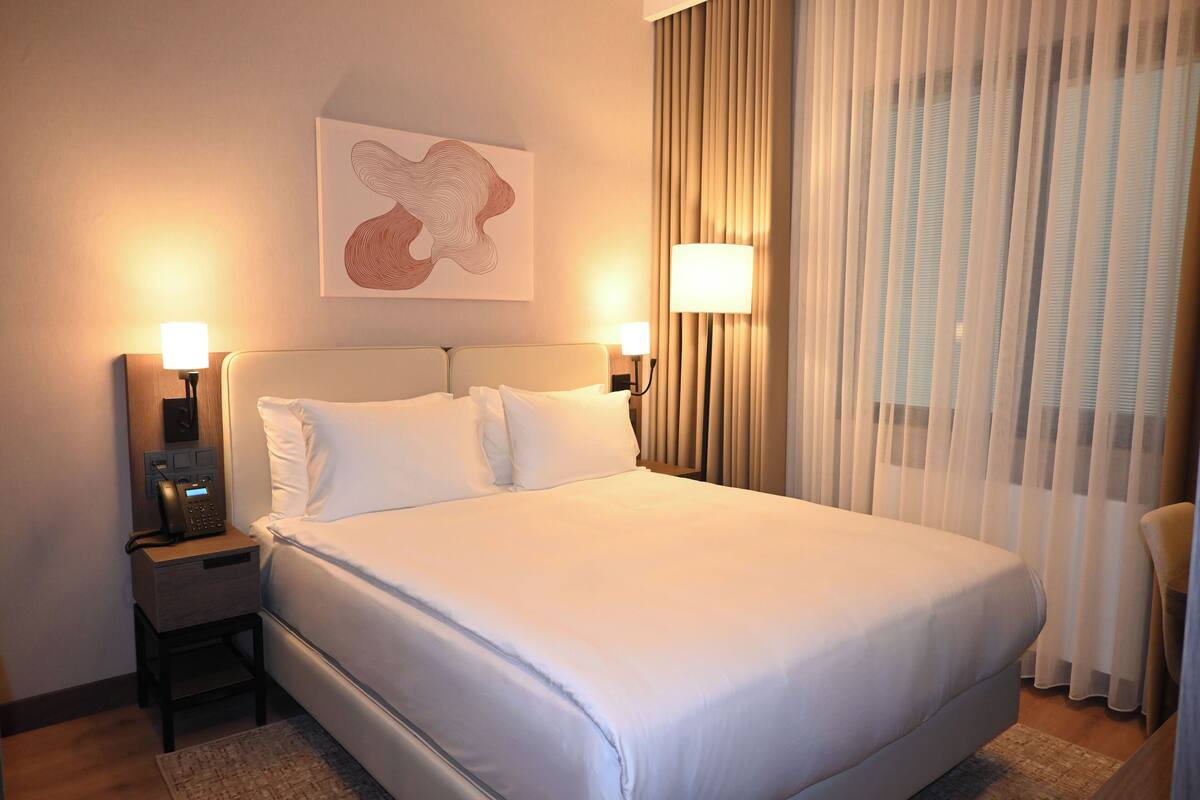 Ein Hotelzimmer mit einem großen Bett, zwei Nachttischlampen, einem Telefon auf dem Nachttisch und einem Gemälde an der Wand.