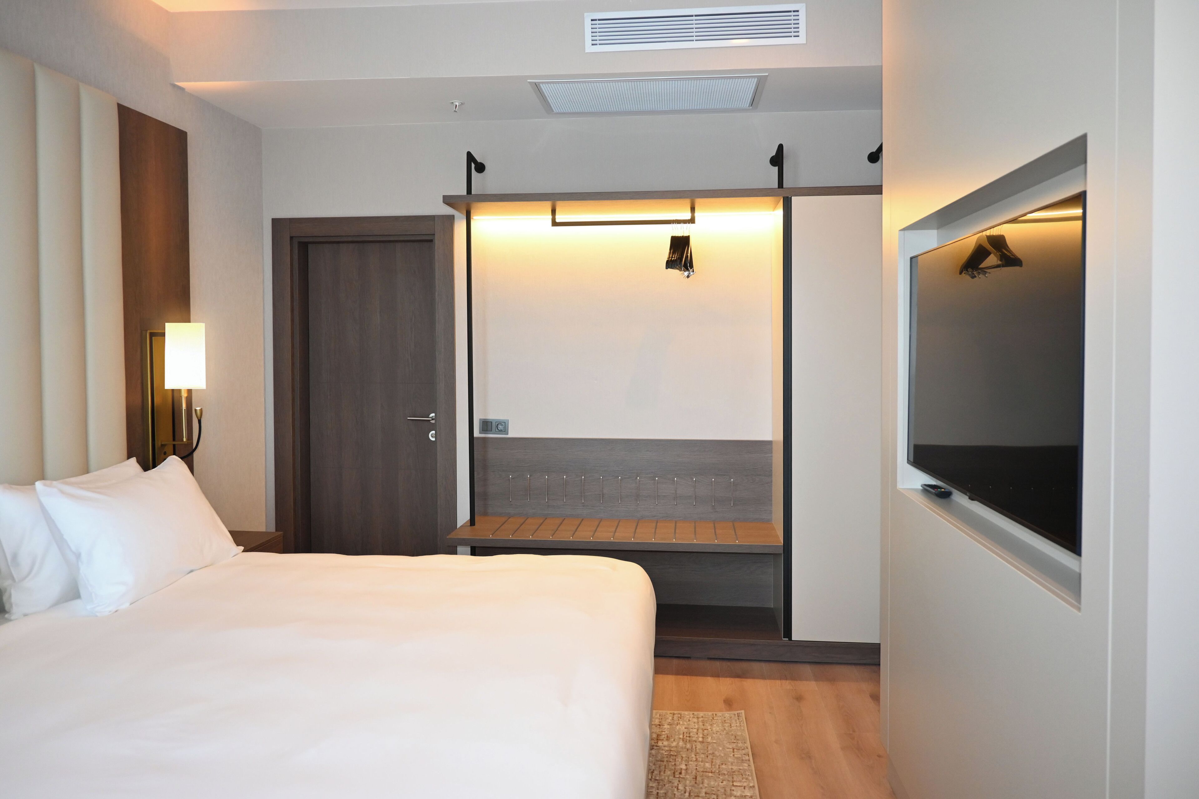 Une chambre d’hôtel avec un lit, un bureau, une télévision, une porte et un luminaire.