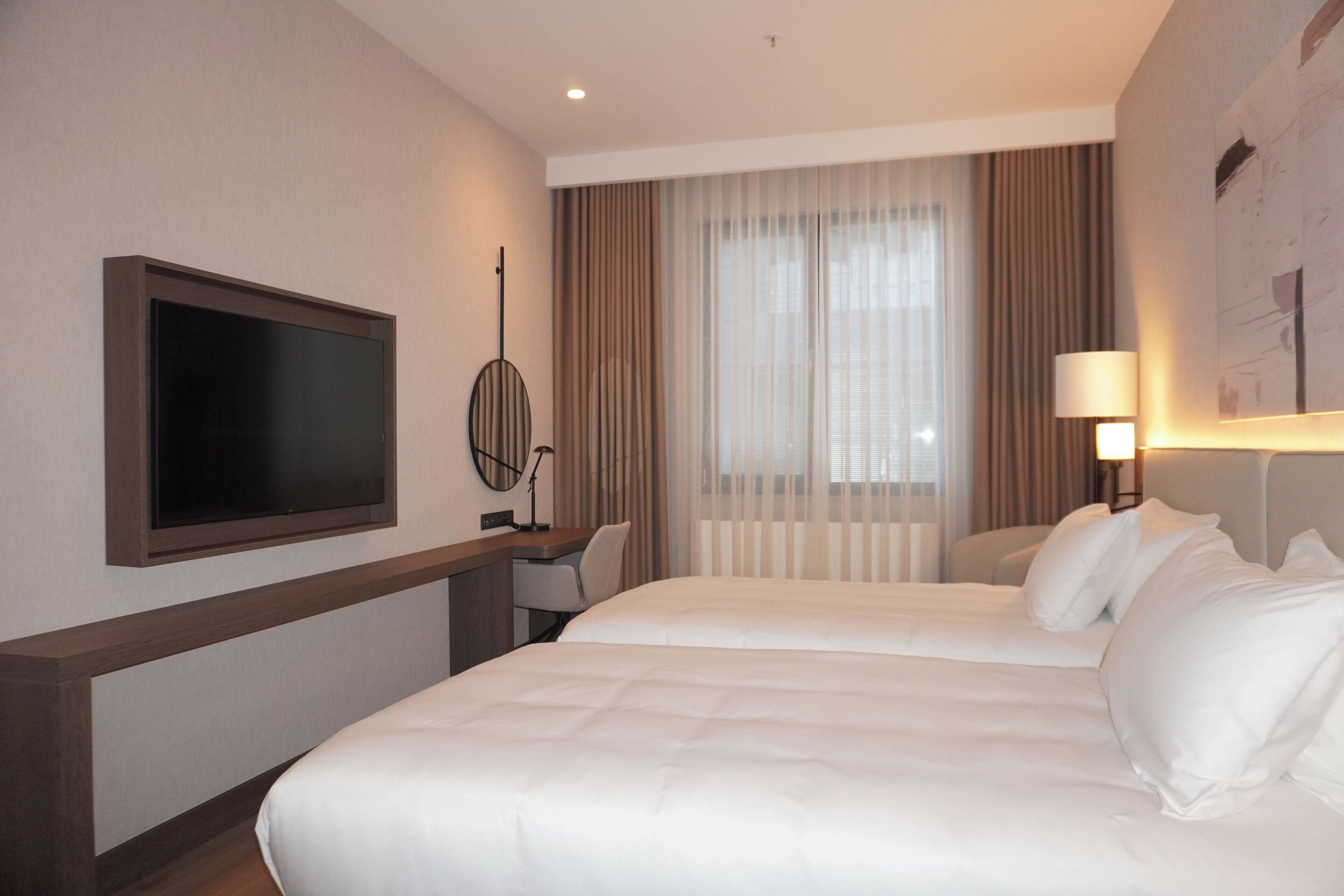 A hotel room with a bed, a desk, a chair, a TV, and a window with curtains.