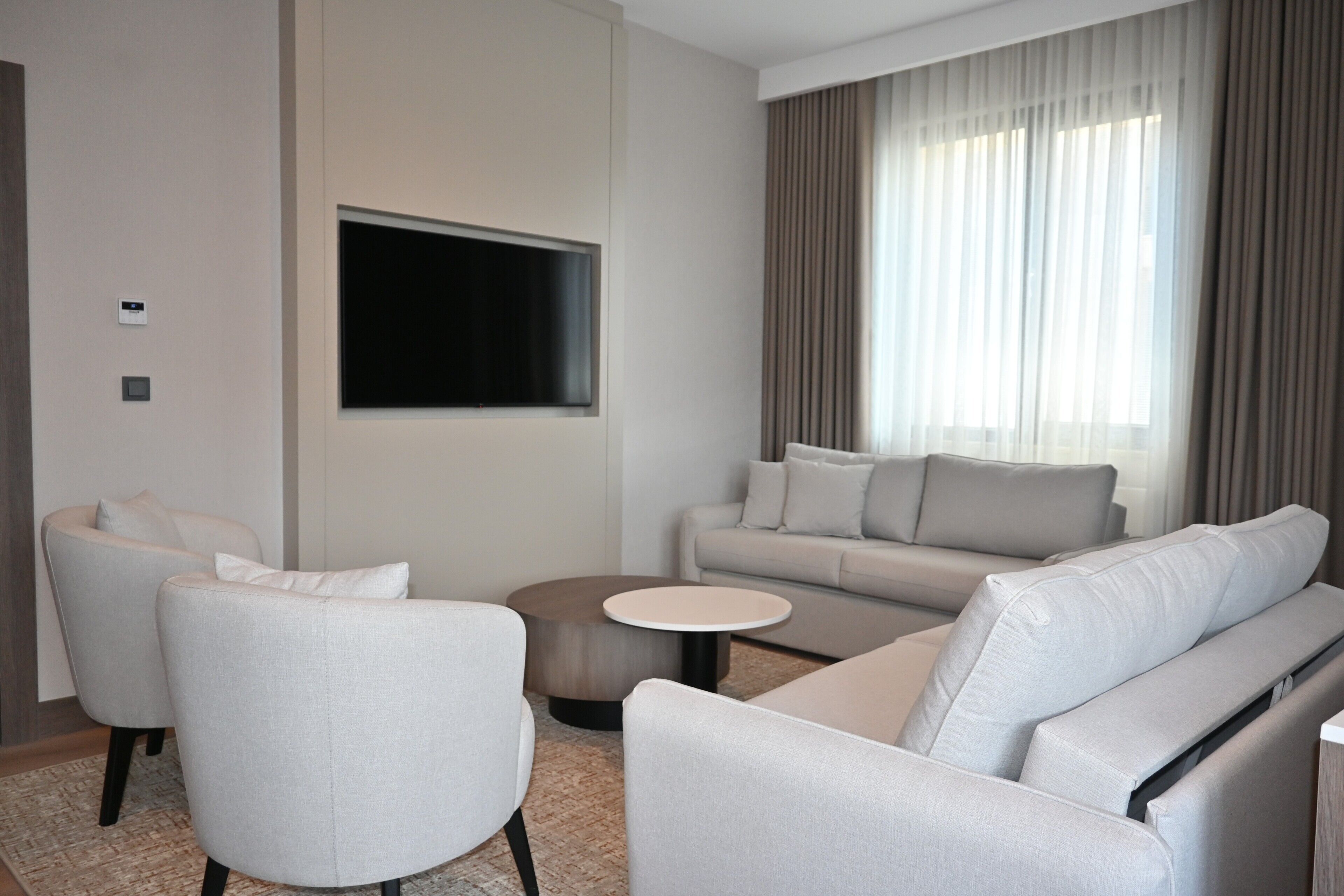 A modern living room with a sofa, armchairs, a coffee table, and a flat-screen TV mounted on the wall.