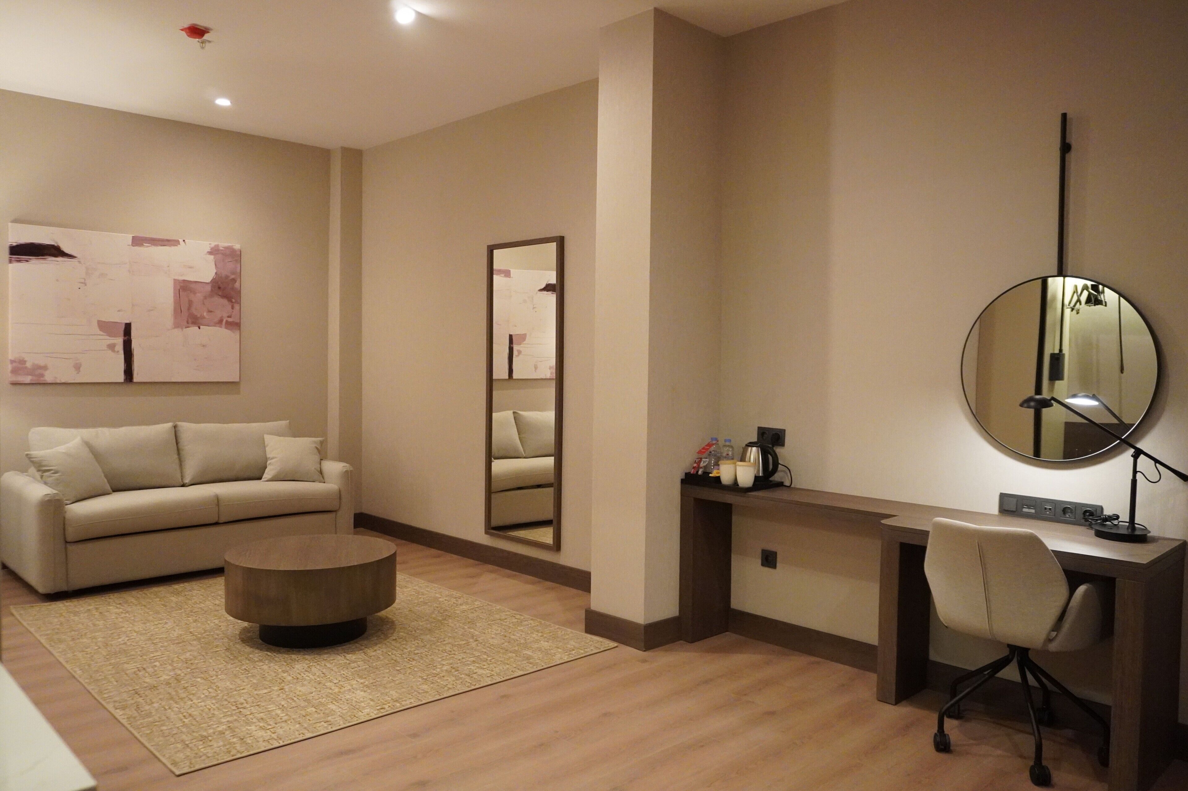 A modern room with a sofa, a round coffee table, a desk with a chair, and a large mirror.
