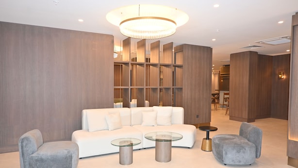 Un interior moderno con un sofá blanco, dos mesas de centro de vidrio y sillones grises.