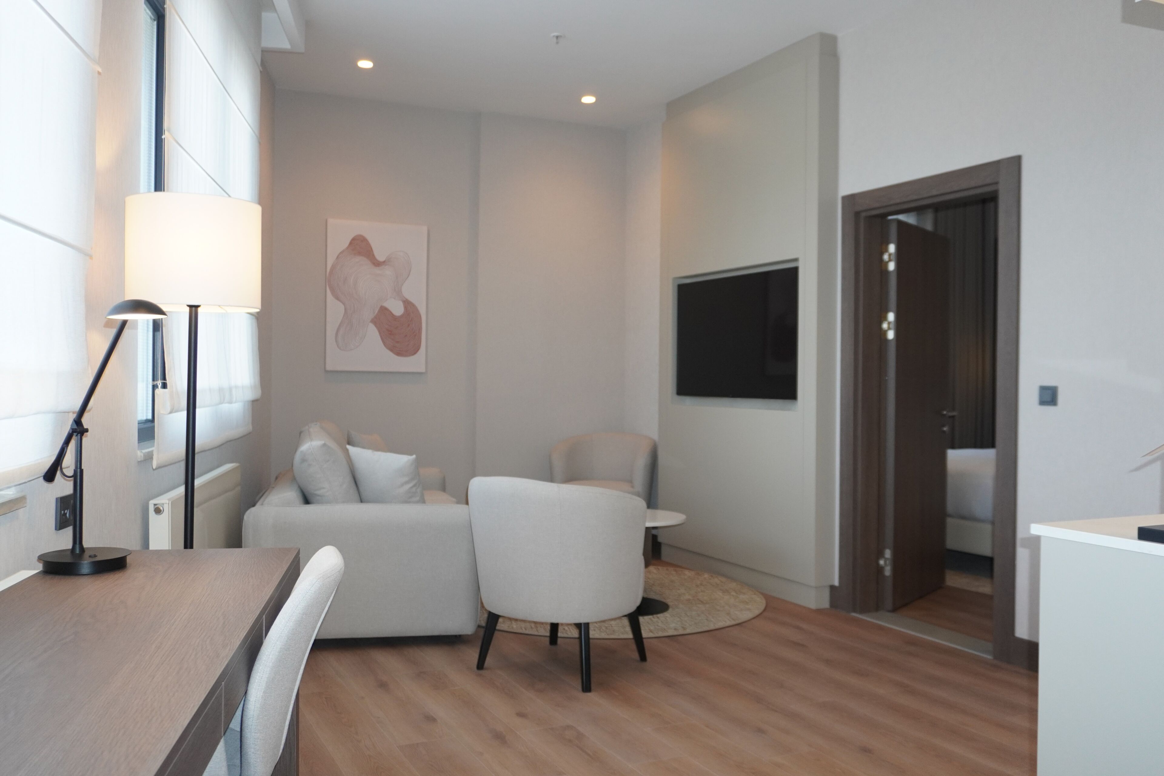 Een moderne kamer met een bank, een stoel, een klein tafeltje, een lamp, een televisie en een deur.