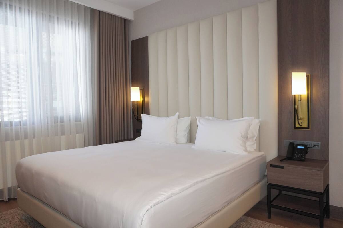 Ein Hotelzimmer mit einem großen Bett, einem Nachttisch mit Lampe, einem Telefon und einer Wandleuchte.