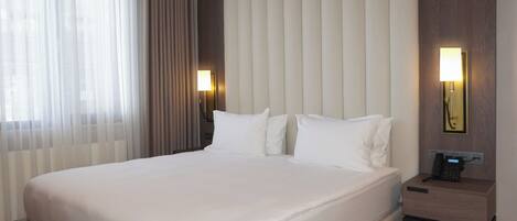 Habitación de hotel con una cama grande, una mesita de noche con lámpara, teléfono e iluminación en la pared.