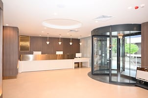 Un área de recepción moderna con mostrador, puerta giratoria de vidrio e iluminación empotrada en el techo.