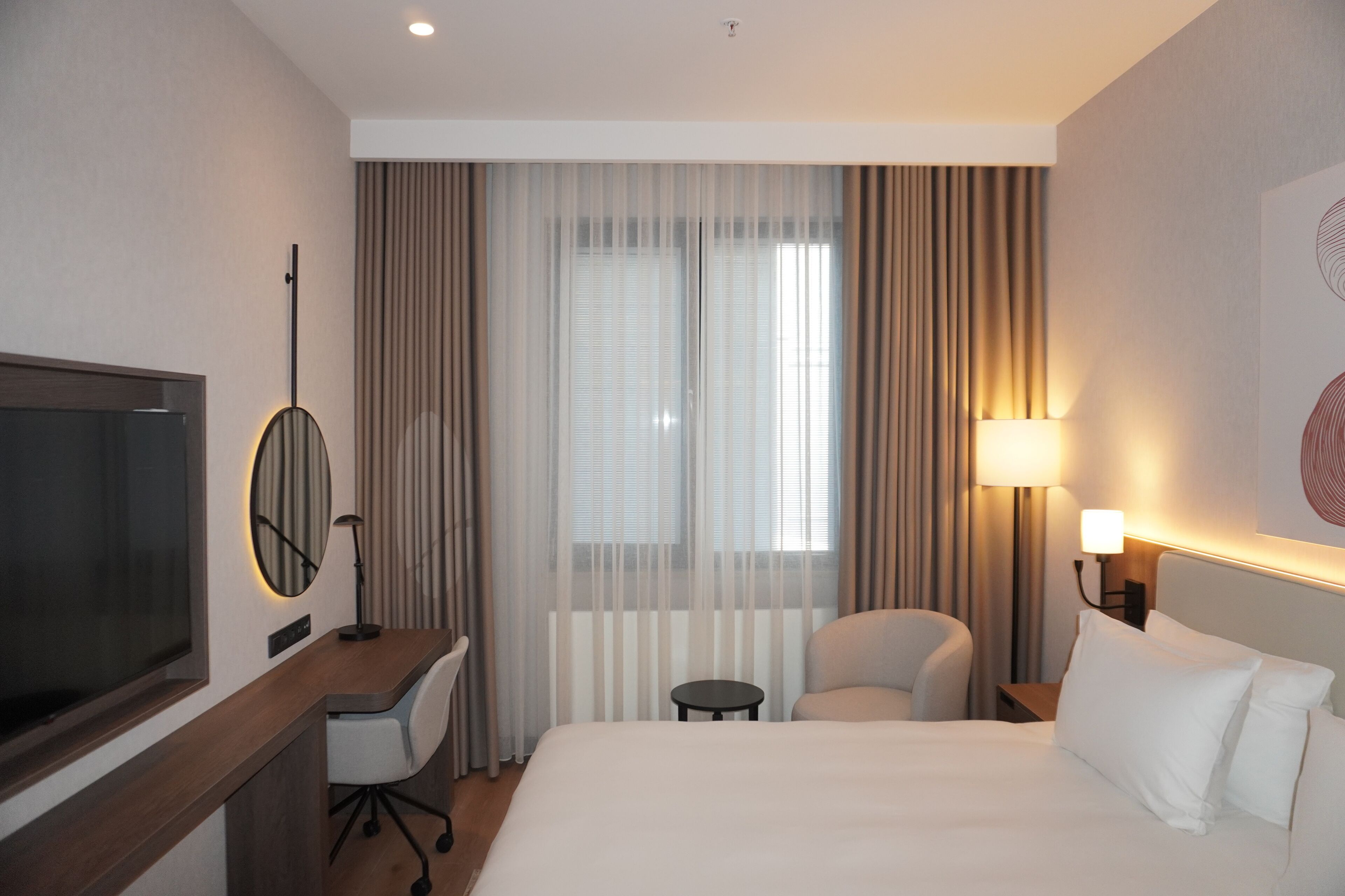 A hotel room with a bed, desk, chair, TV, and curtains.