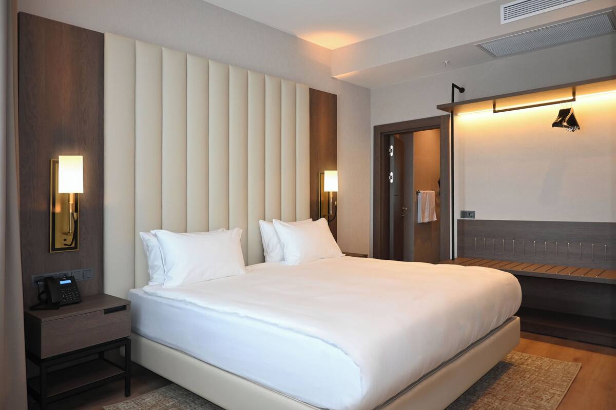 Ein Hotelzimmer mit einem großen Bett, Nachttischlampen, einem Nachttisch, einem Spiegel und einem Kleiderschrank.