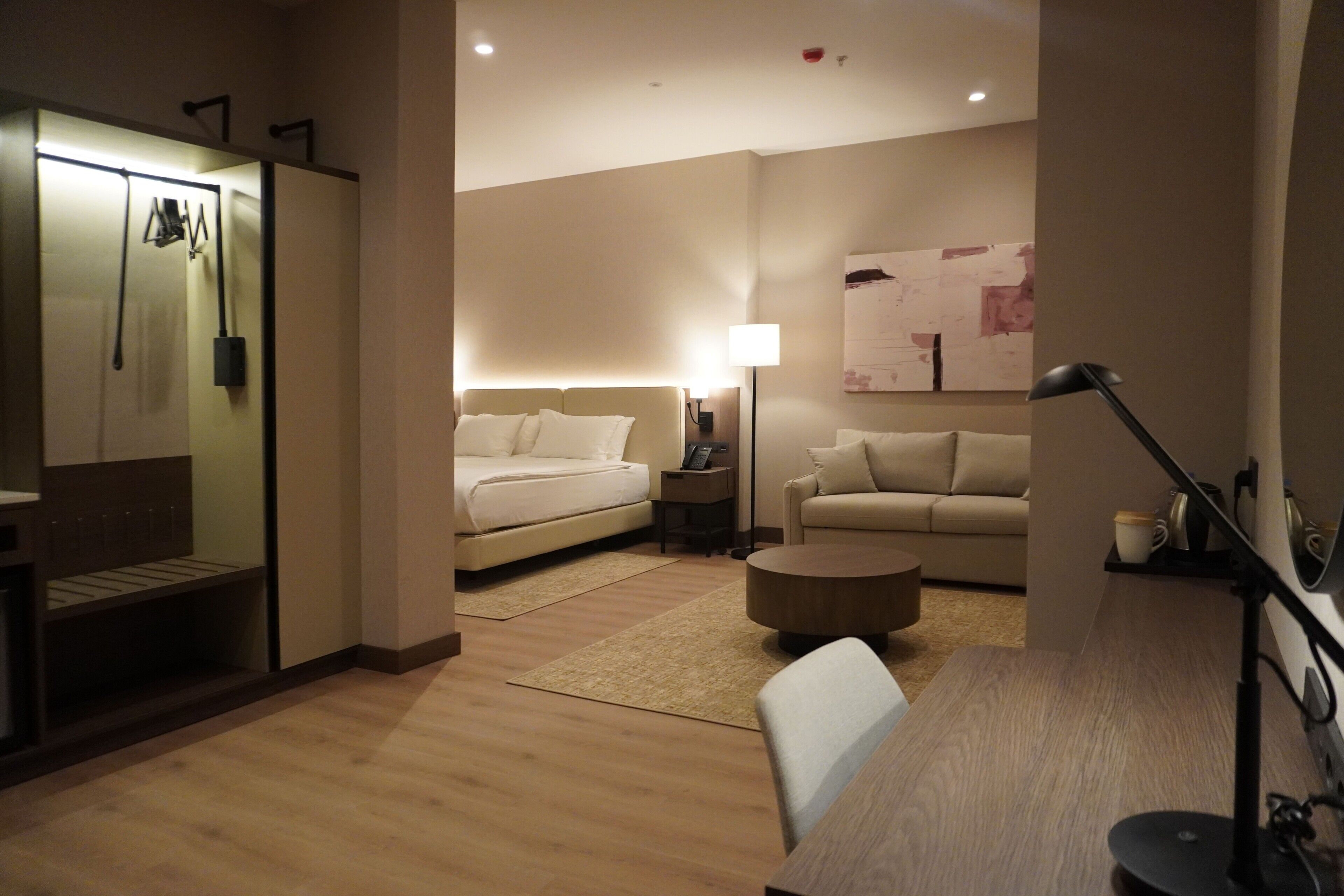 Una habitación de hotel moderna con cama, sofá, mesa de centro, escritorio y lámpara.