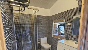 Baño con ducha, inodoro y lavamanos, con baldosas estampadas en blanco y negro y un trave de madera en el techo.