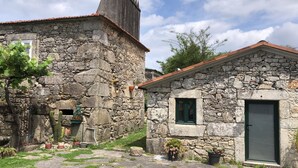 Un edificio de piedra con puerta, ventanas y un pequeño jardín con plantas en macetas.