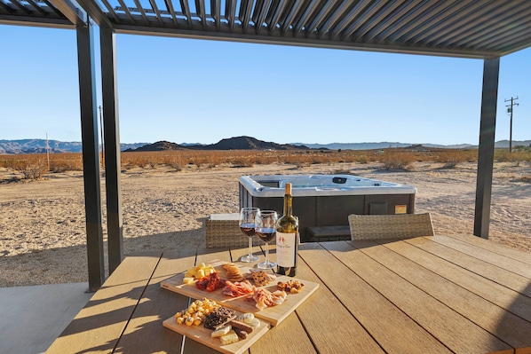 Eine Terrassenanlage im Freien mit Whirlpool, einem Holztisch mit Speisen und Wein sowie einer Wüstenlandschaft im Hintergrund.