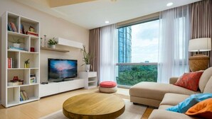 A modern living room with a flat-screen TV, a round coffee table, a sofa, and a bookshelf. - Modern Luxe Stay: 2BR City Escape (Taguig City)