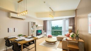 A modern living room with a dining area, a television, and a large window with a city view. - Modern Luxe Stay: 2BR City Escape (Taguig City)