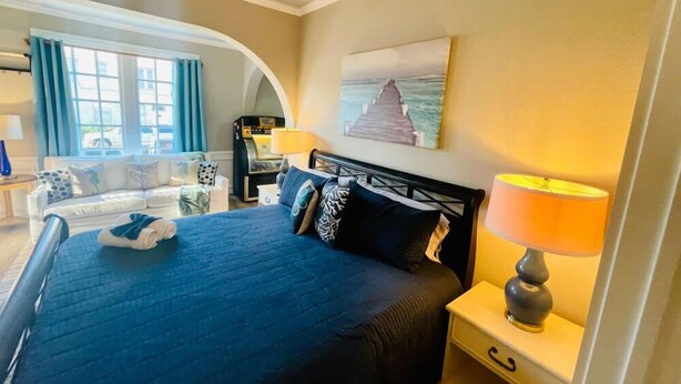 Een hotelkamer met een bed, een nachtkastje met een lamp, een schilderij aan de muur en uitzicht op de omgeving door een raam.