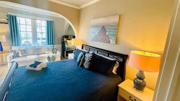 A hotel room with a bed, a nightstand with a lamp, a painting on the wall, and a view of the outdoors through a window.