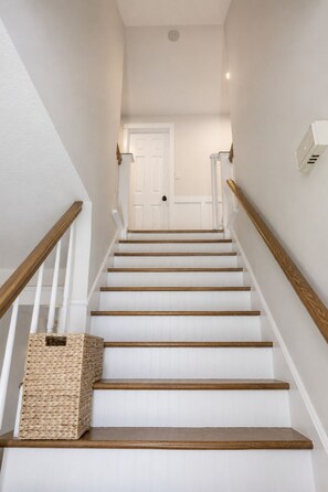 Eine Treppe mit weißen Wänden, Holzhandläufen und einem Korb unten.