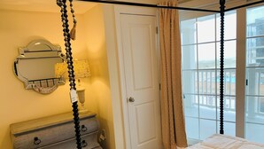 Ein Schlafzimmer mit Himmelbett, einem Schminktisch mit Schubladen, einem Spiegel, einer Lampe und einer Tür zum Balkon.