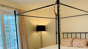 Ein Bett mit Baldachin, mit weißer Bettdecke, eine schwarze Wandlampe und ein Fenster mit Vorhängen.