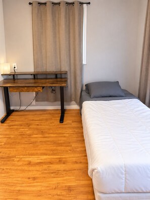 A bedroom with a wooden desk, a bed with white bedding, and a window with curtains.