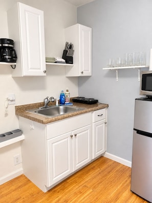 A compact kitchen with white cabinets, a granite countertop, a stainless steel sink, a coffee maker, a toaster, and a microwave.