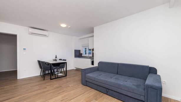 A modern living room with a grey sofa, a dining table with chairs, and a kitchen area in the background. - Altiora Prestige Residence 201 (Gradac)