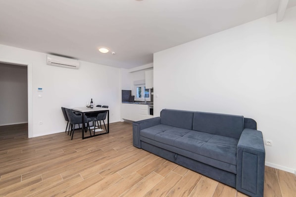 A modern living room with a grey sofa, a dining table with chairs, and a kitchen area in the background. - Altiora Prestige Residence 201 (Gradac)