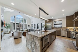 A modern kitchen with a large island, stainless steel appliances, and a dining area with a sofa and chairs. - Stateline Designer Luxury Home (South Lake Tahoe)