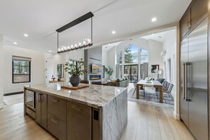 A modern kitchen with a marble island, stainless steel appliances, and a dining area with a view. - Stateline Designer Luxury Home (South Lake Tahoe)