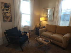 A living room with a sofa, a chair, a coffee table, a lamp, and a window with curtains.