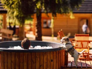 Un bain Ă remous en bois, avec un chien debout sur le bord.