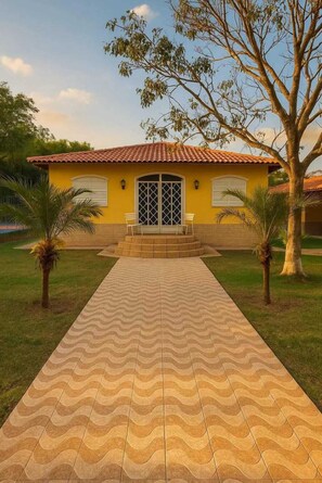A yellow building with a tiled roof, a central entrance, and a paved walkway leading to it. - Country house in Cruzeiro, SP, with pool, gourmet area and leisure facilities near Canção Nova. (Cruzeiro)