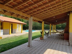 Zona exterior coberta amb piscina, edifici groc i cadira de balanç.