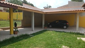 A covered outdoor area with a car parked inside, surrounded by a yellow wall and a tiled roof.