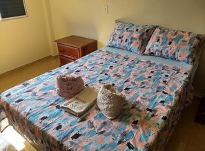 A bed with a patterned bedspread, a pillow with text, a small wooden nightstand, and a wall socket. - Country house in Cruzeiro, SP, with pool, gourmet area and leisure facilities near Canção Nova. (Cruzeiro)