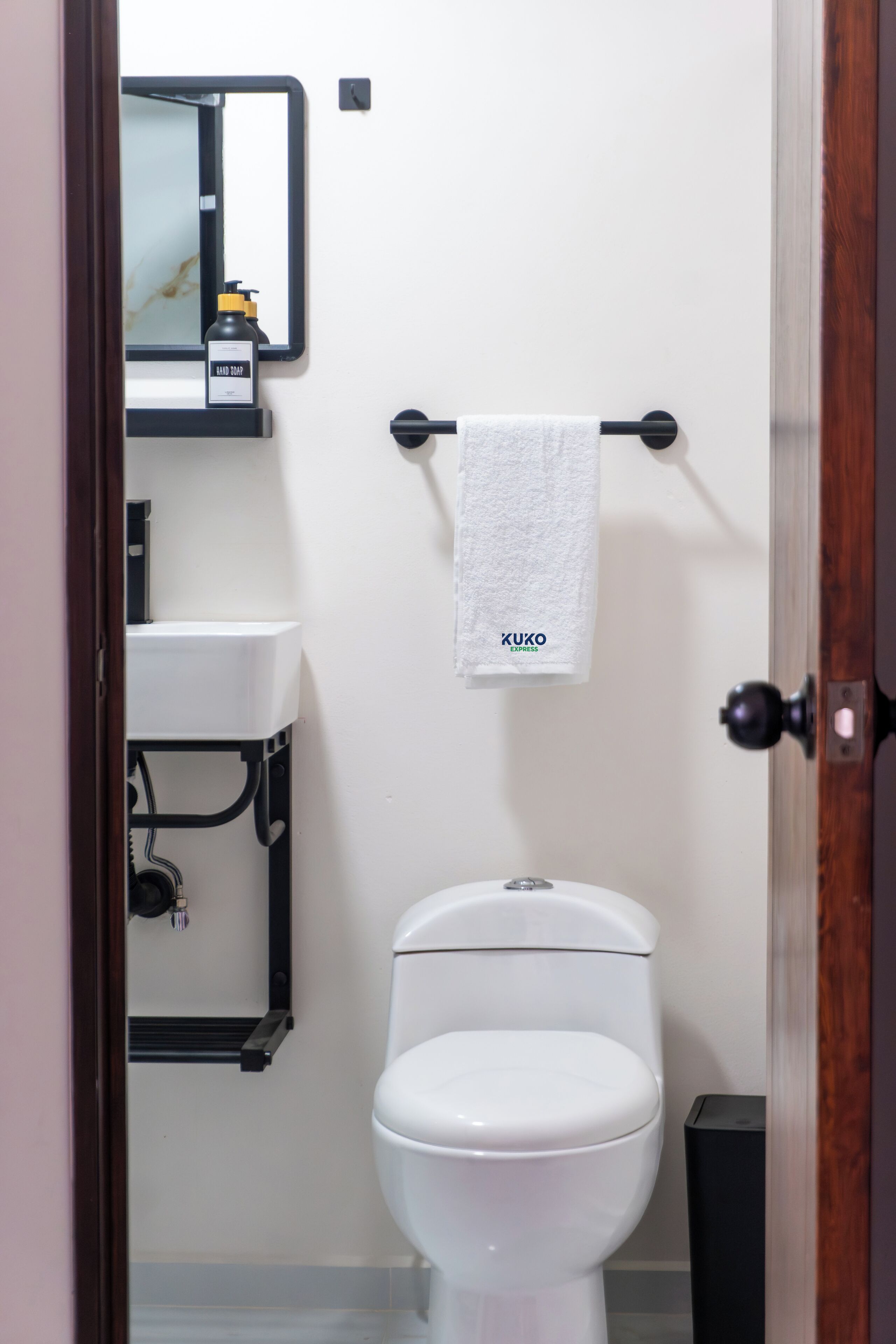 A bathroom with a white toilet, a sink, a mirror, and a towel rack with a towel.