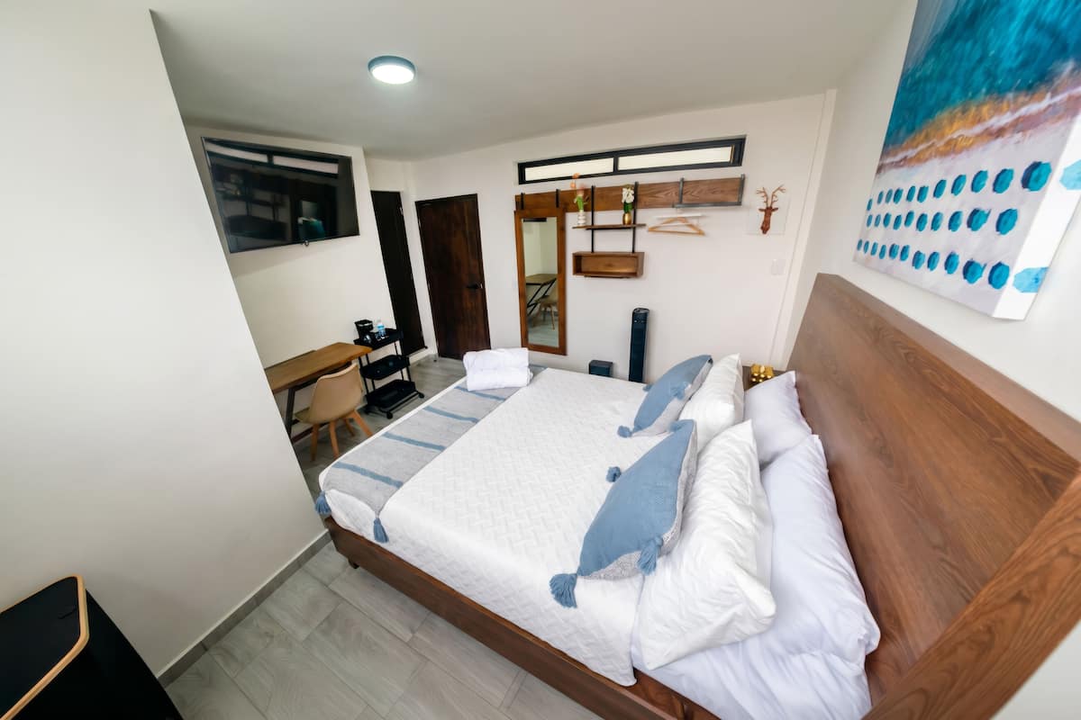 Moderni hotellihuone, jossa on suuri sänky, työpöytä, tuoli, vaatekaappi ja taulu seinällä.
