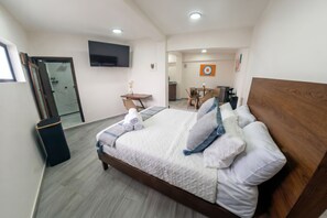 A hotel room with a bed, a desk, a chair, a TV, and a target artwork on the wall.
