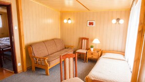 A room with a wooden floor, a bed, a sofa, a chair, a small table with a lamp, and two wall-mounted lights. - Cottage for 5 People, Wapnica (Międzyzdroje)