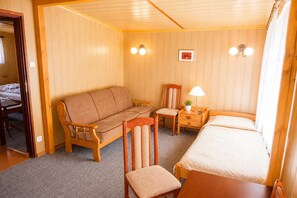 Ein Zimmer mit Holzboden, einem Bett, einem Sofa, einem Sessel, einem kleinen Tisch mit Lampe und zwei Wandleuchten.