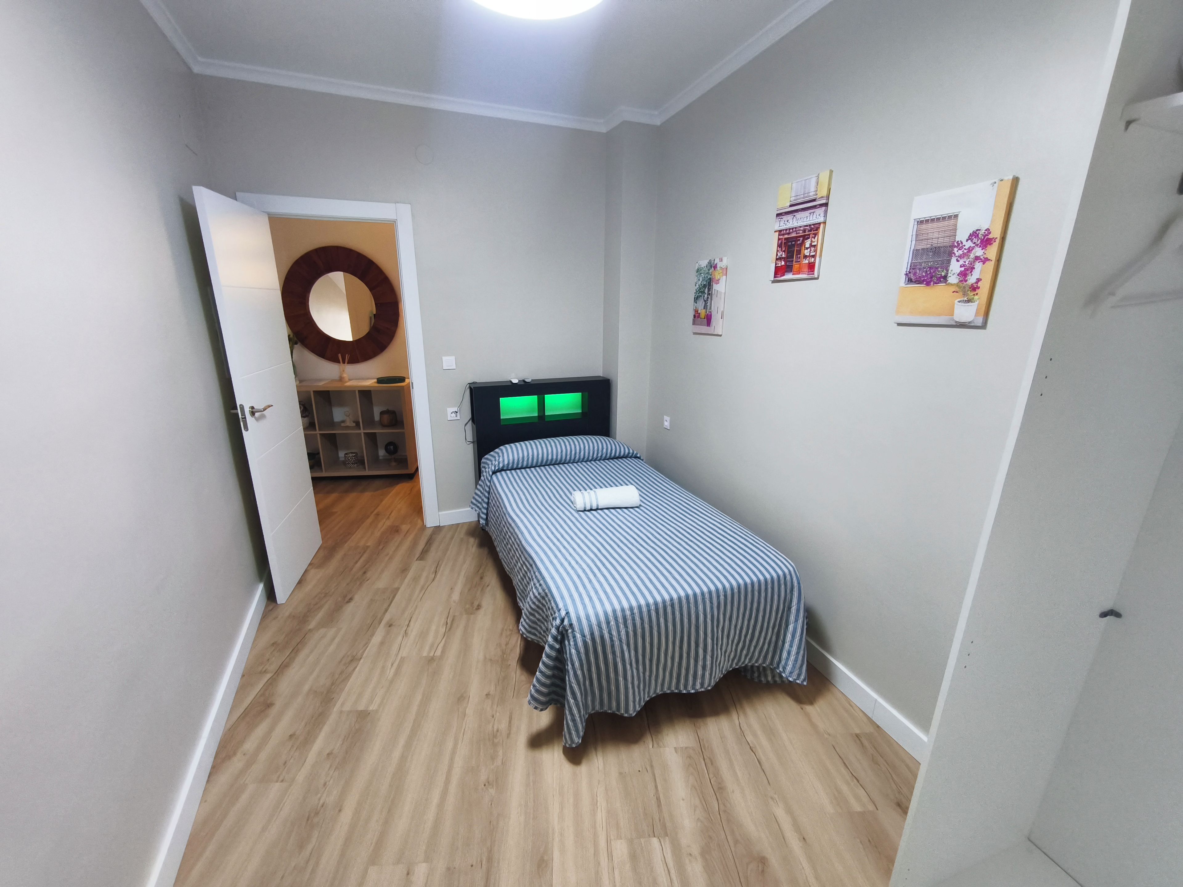 A small, neatly arranged bedroom with a single bed, a wooden floor, and a door leading to a bathroom.