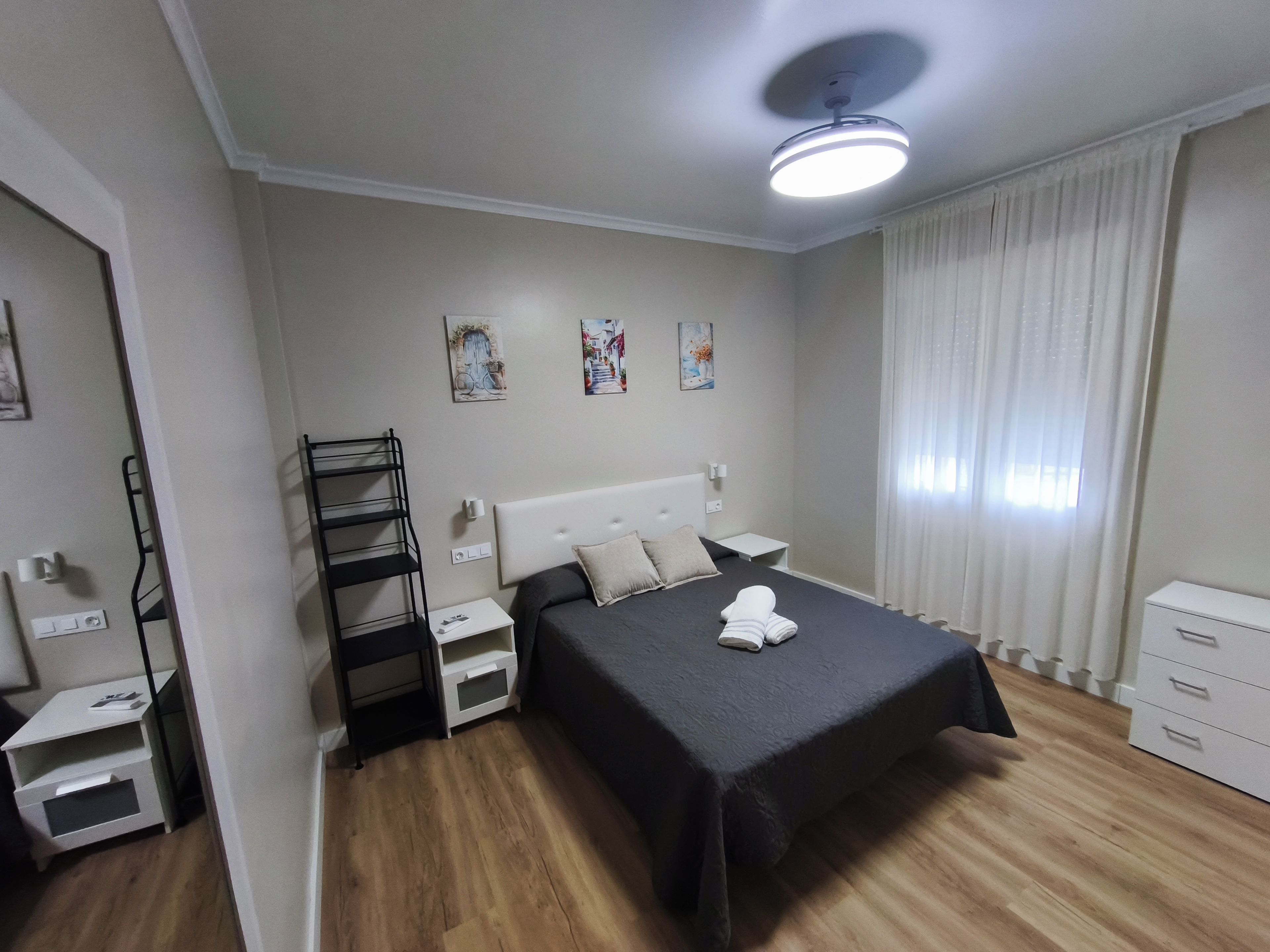 A bedroom with a bed, bedside tables, a nightstand, a ceiling fan, and a window with curtains.