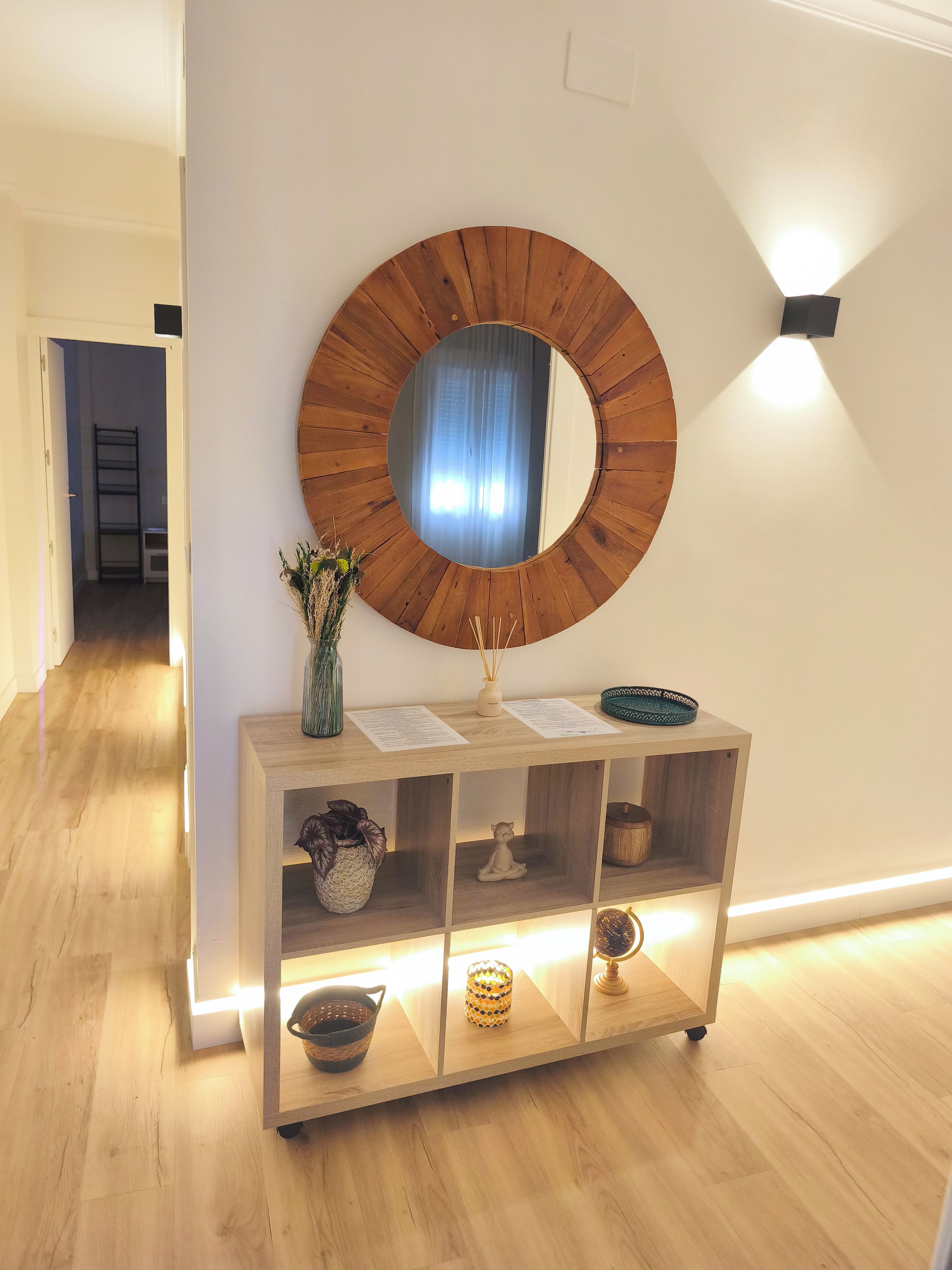 A modern interior with a wooden console table, a round mirror, and a wall-mounted light fixture.