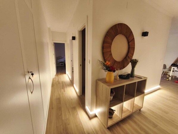 A hallway with wooden flooring, a wooden console table with a mirror, and a door with a key lock.