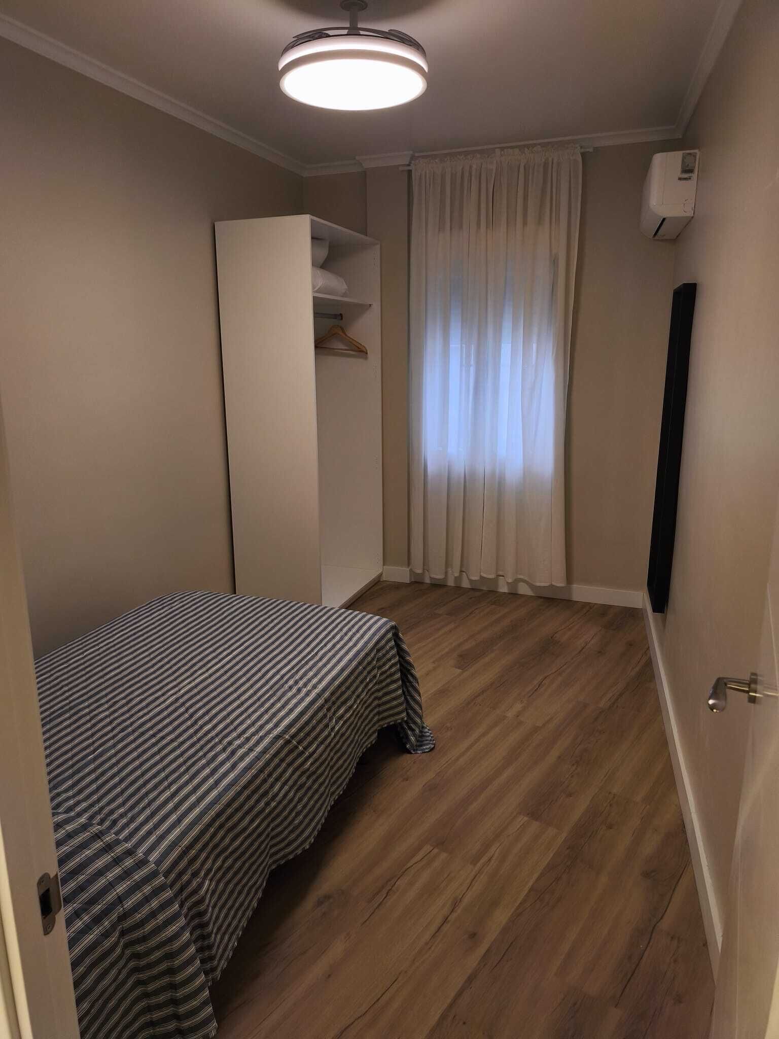 Une petite pièce comprenant un lit, une armoire, une fenêtre avec des rideaux et un appareil de climatisation.