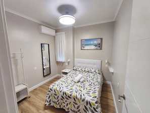 Et soveværelse med seng, natbord, spejl, klimaanlæg, et billede og en loftlampe.
