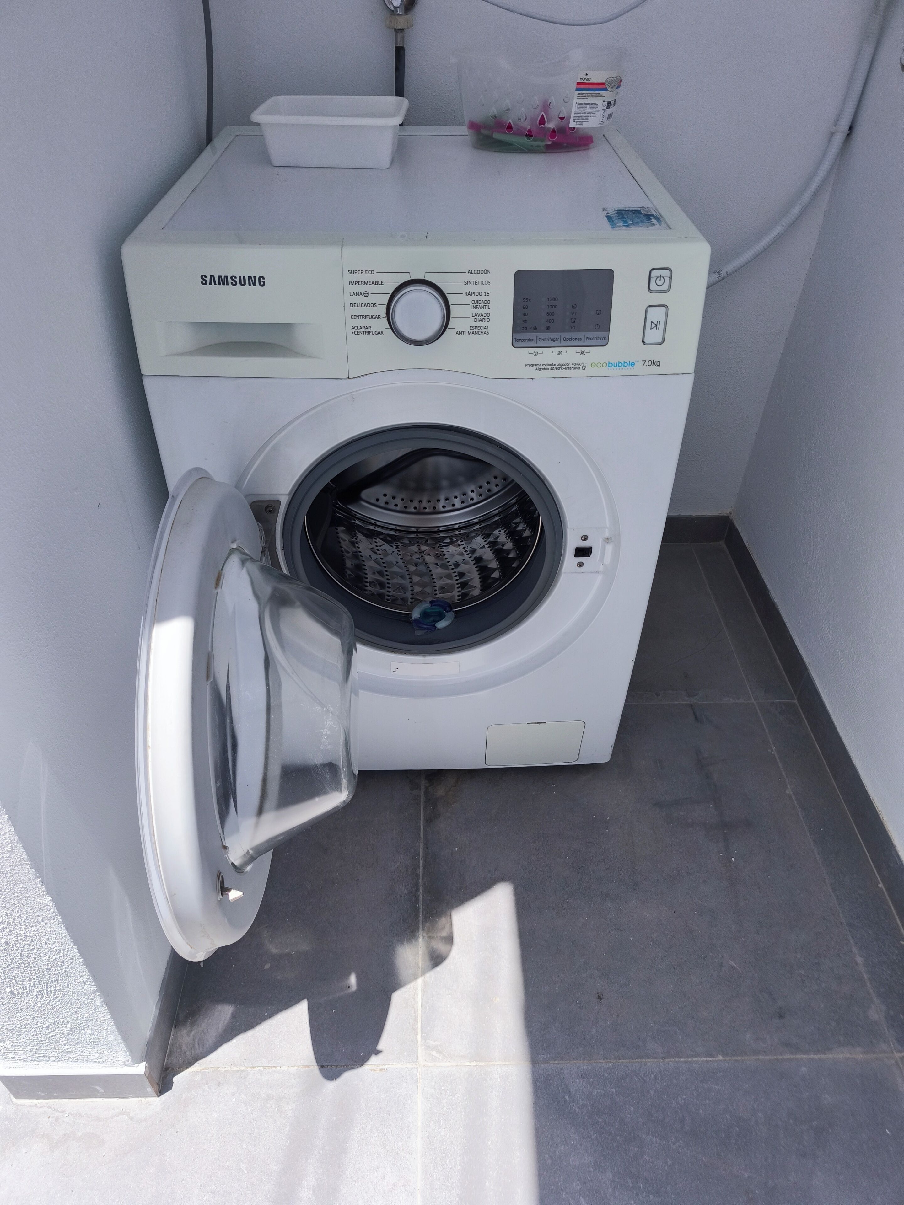 A Samsung front-loading washing machine in a corner with a tiled floor.