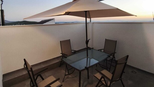 Una terraza en la azotea con una mesa y sillas de vidrio, un paraguas y vistas al horizonte de la ciudad.