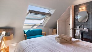 A bedroom with a skylight, a bed, a blue chair, and a bathroom with a mirror and sink. - Guest Room "Escale Sauzonnaise - La Baie" with Sea View, Shared Pool and Wi-Fi (Sauzon)