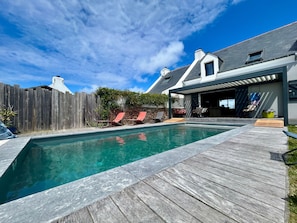 Une piscine avec une terrasse en bois, un patio couvert et une cour arrière clôturée.